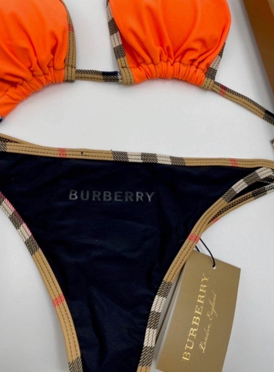 Burberry bikini set with orange bottom and navy top on a white surface.